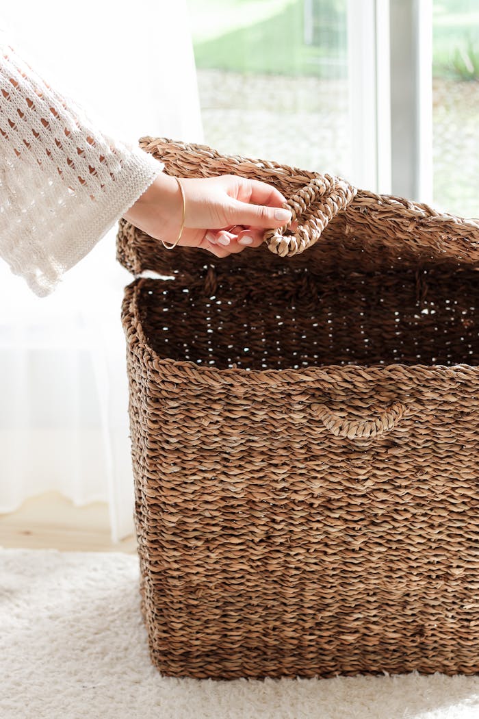 who-we-are Hand opening a woven wicker basket in a sunlit indoor space, suggesting organization and home decor.