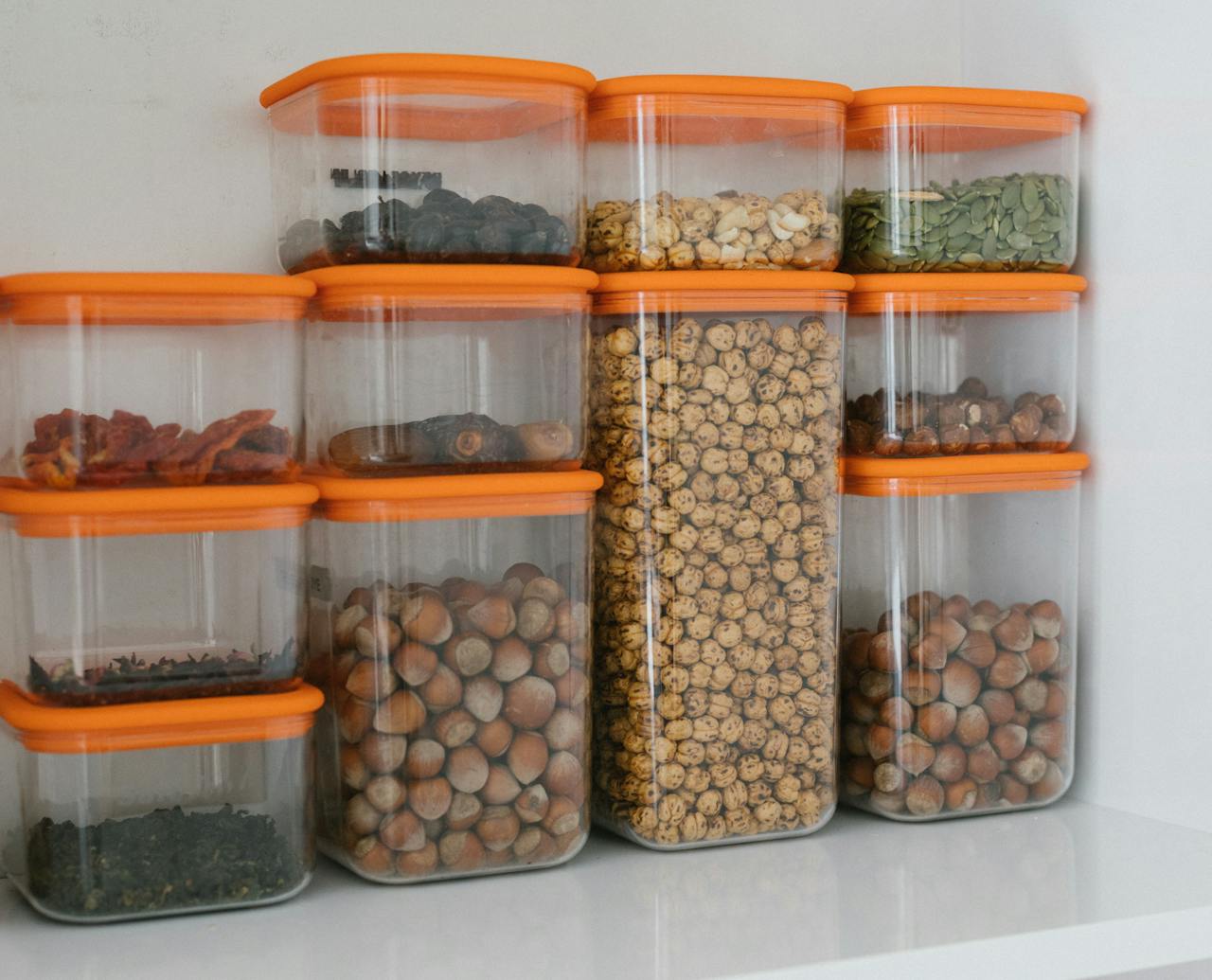 services-03 Various nuts and grains stored in transparent plastic containers with orange lids, organized neatly.